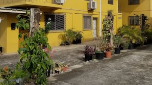A yellow building with multiple windows, air conditioning units, and a balcony with a metal railing.