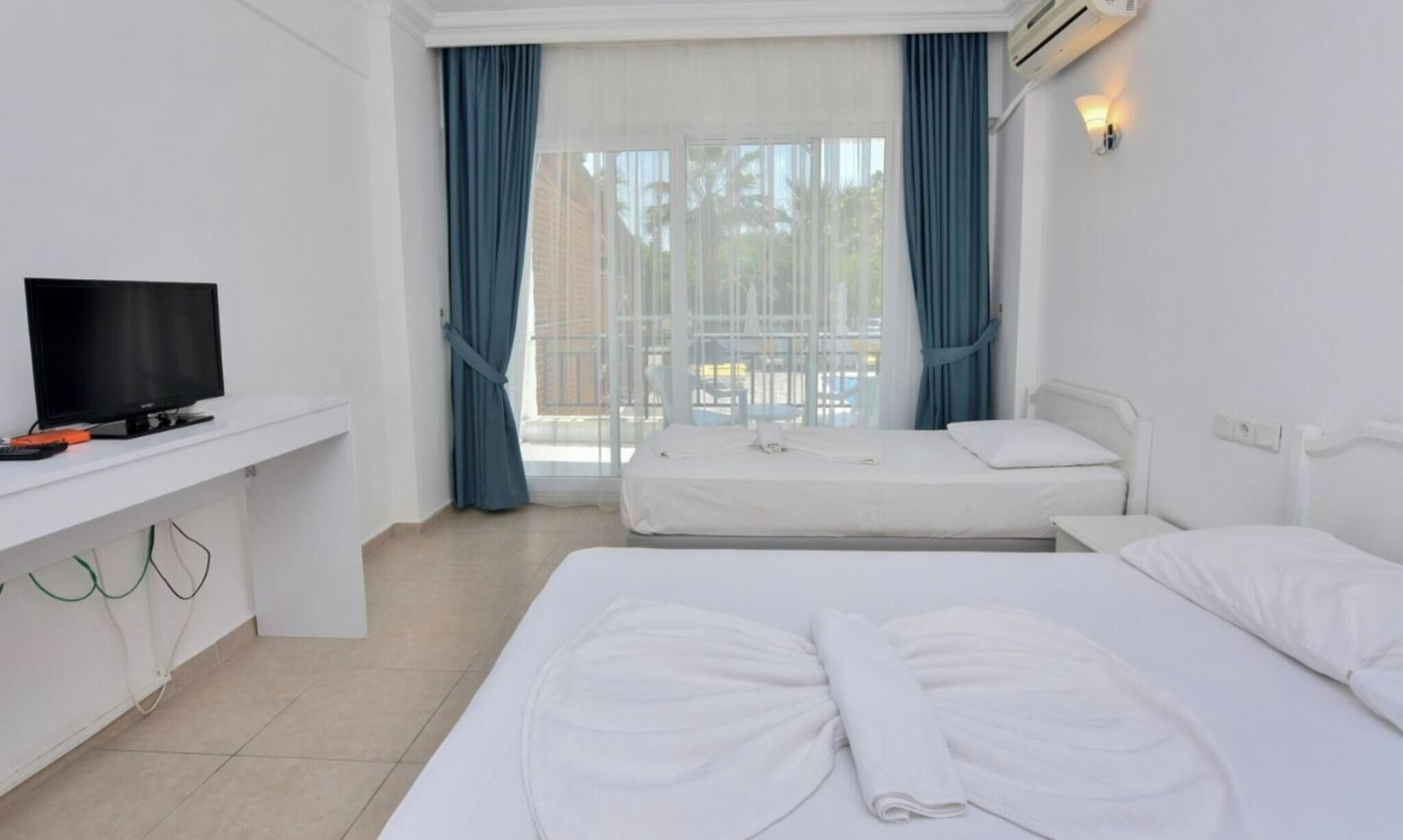 A hotel room with a TV, two beds, a window with curtains, and an air conditioning unit.