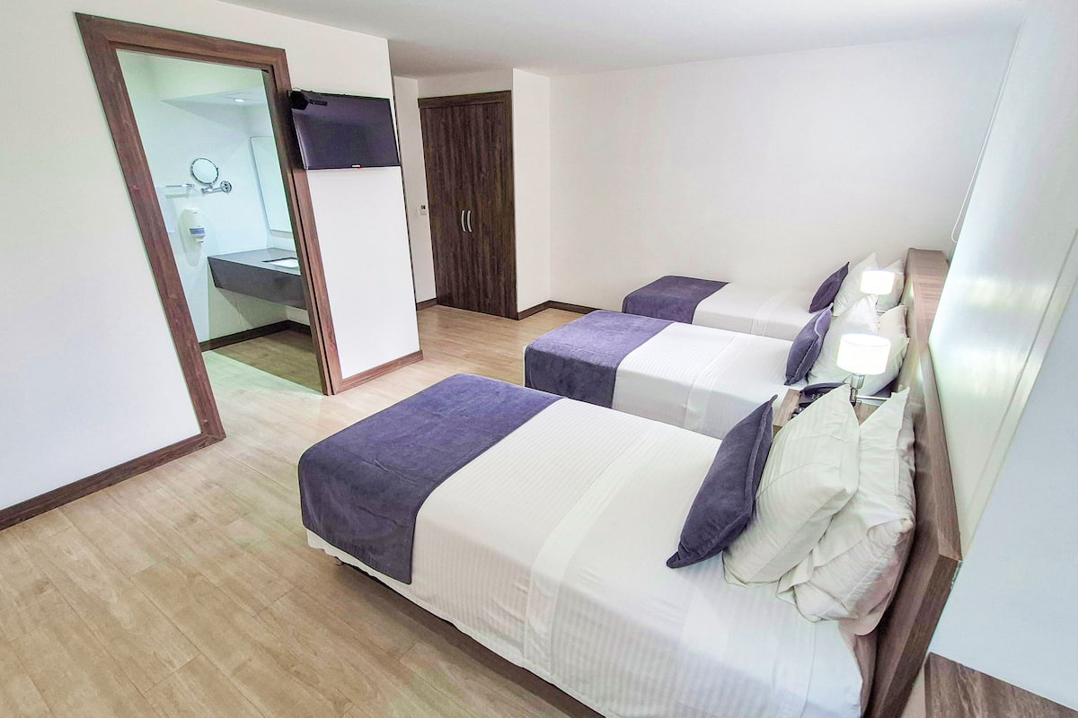 A hotel room with two beds, a bathroom, and a TV mounted on the wall.