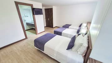 Quarto de hotel com duas camas, banheiro e televisão fixada na parede.