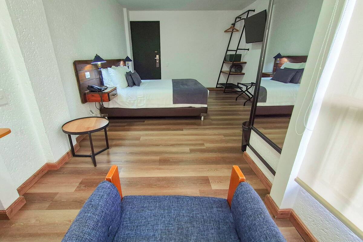 A hotel room with a bed, a small round table, a chair, and a TV mounted on the wall.