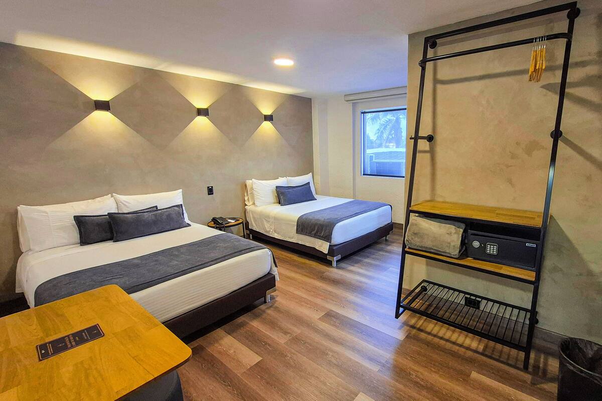 A modern hotel room with two beds, a small table, a wardrobe, and a window with a view.