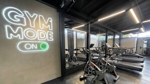 Un gimnasio con un letrero de neón que dice 'GYM MODE ON' y equipo de ejercicio.
