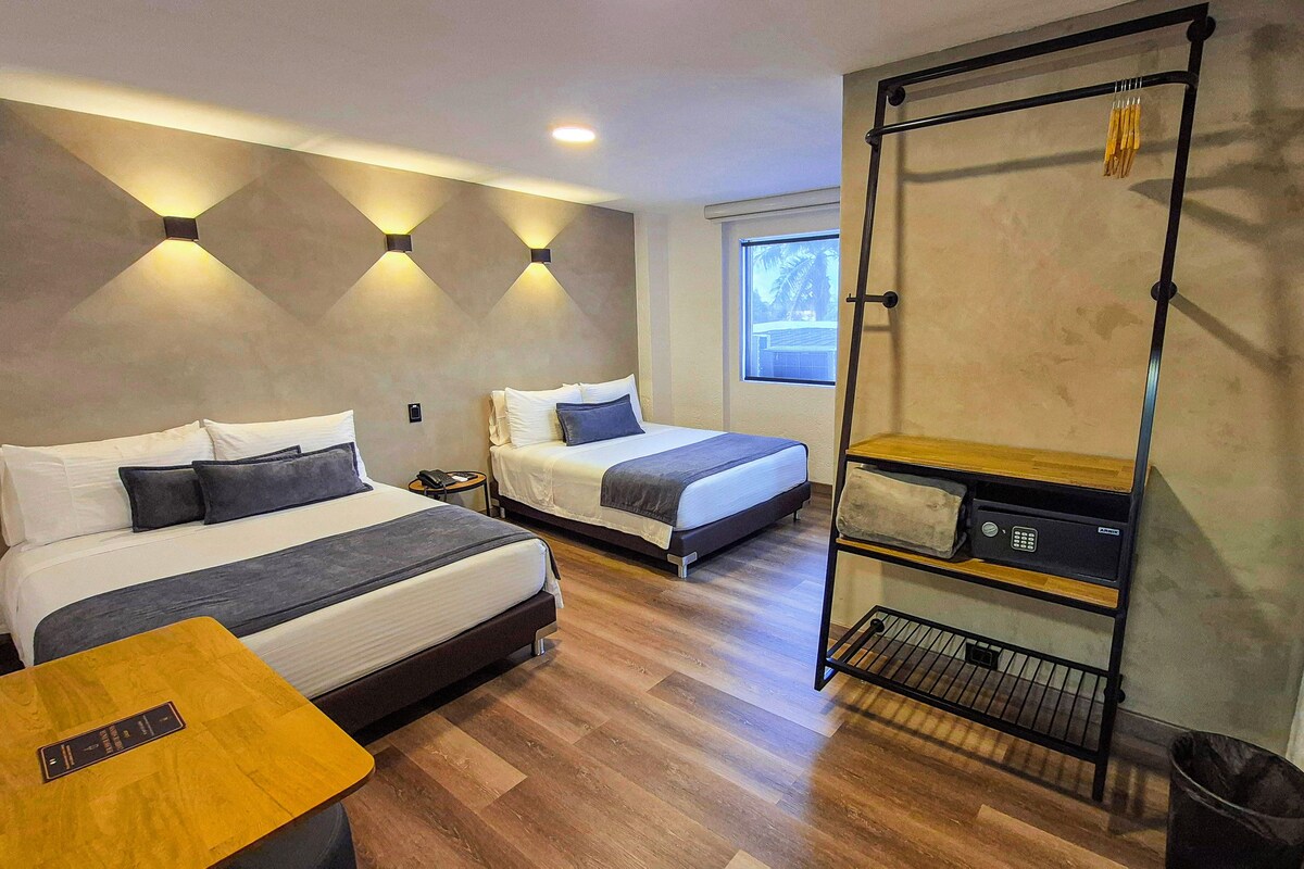 Una habitació d'hotel moderna amb dos llits, una taula petita, un armari i una finestra amb vistes.