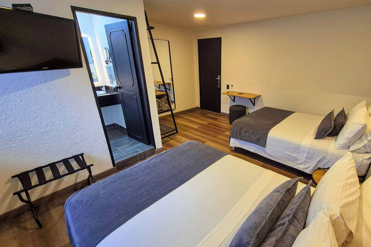 A hotel room with two beds, a bench, a desk, and a door leading to a bathroom.