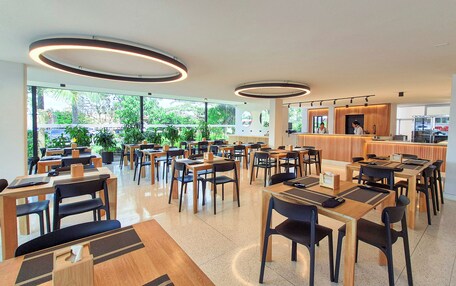A modern restaurant with multiple tables and chairs, a counter with staff, and large windows with a view of greenery.