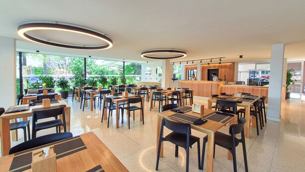 Un restaurante moderno con varias mesas y sillas, una barra de atención y grandes ventanales con vistas a zonas verdes.