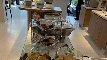 A breakfast buffet with various pastries and bread, a coffee machine, and a TV in the background.