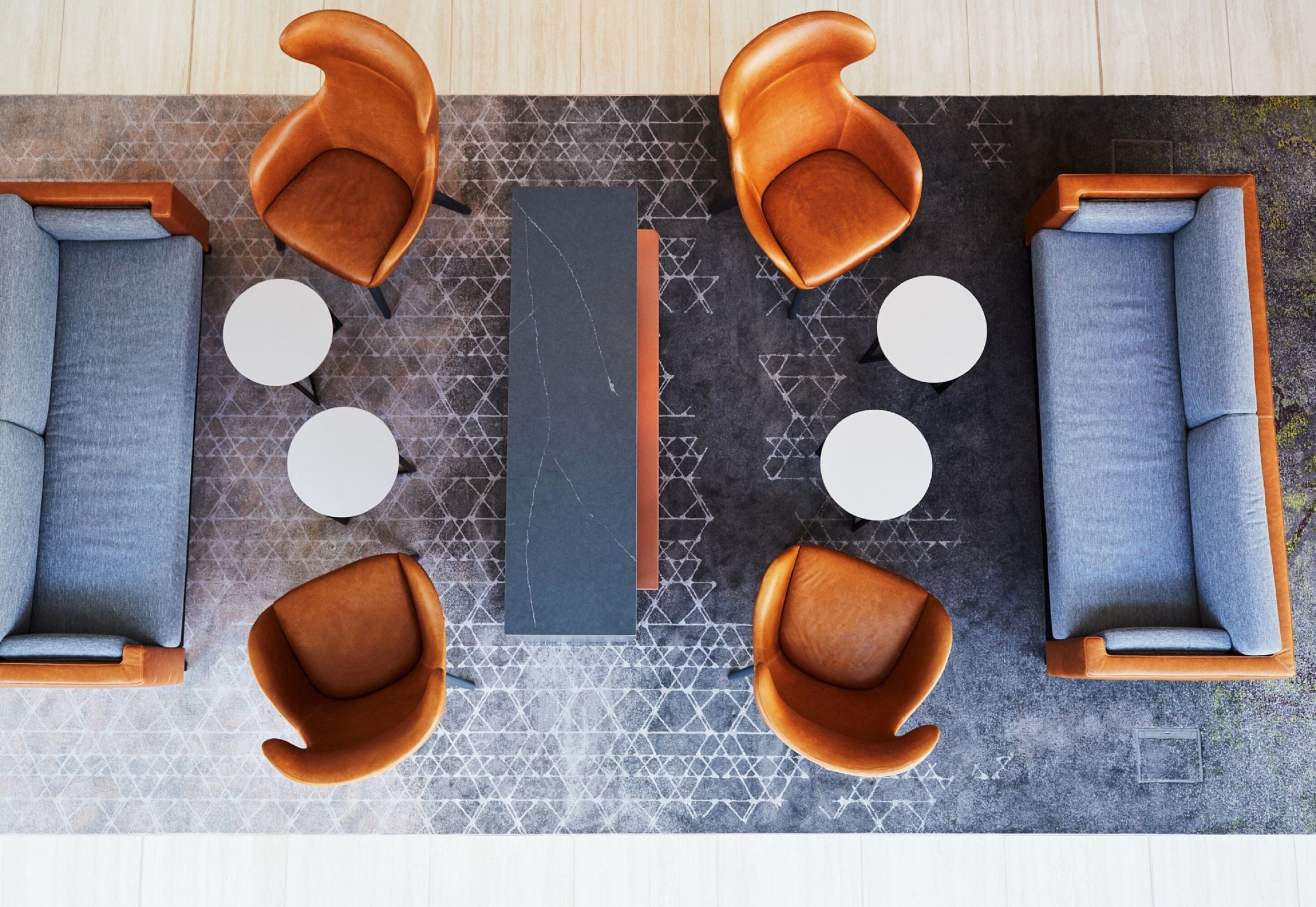 A modern lounge area with sofas, chairs, and a central table, featuring geometric patterned flooring and a neutral color palette.