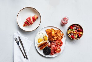 A breakfast plate with eggs, sausages, beans, tomatoes, and a croissant.