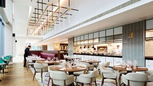 A modern restaurant with round tables, chairs, and a bar area. - Hyatt Regency Manchester (Manchester)