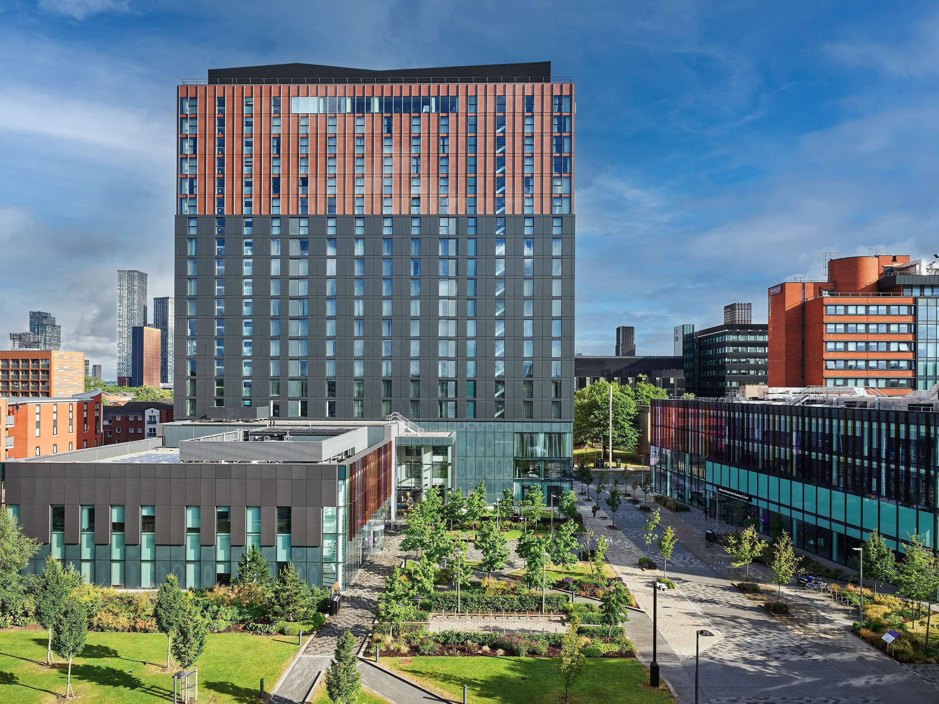 A modern high-rise building with a mix of glass and brick facade, surrounded by a landscaped courtyard with trees and pathways.