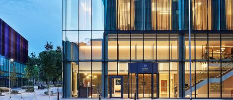 Un hôtel moderne doté d’une façade en verre, d’une entrée bien visible et d’un escalier menant aux étages supérieurs.