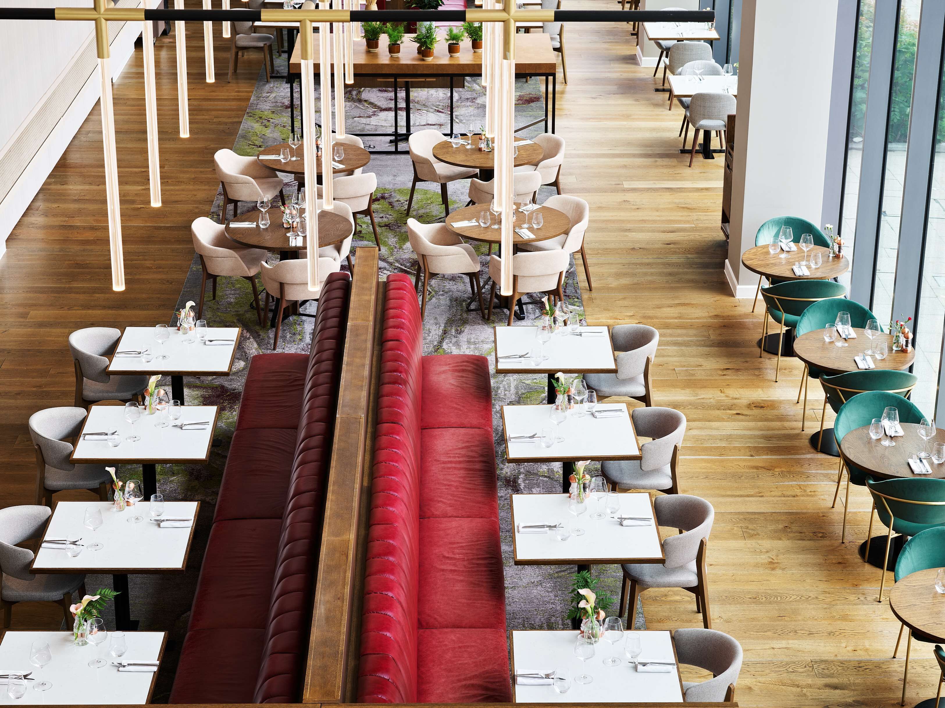 A modern restaurant with wooden flooring, round tables, and cushioned seating areas.