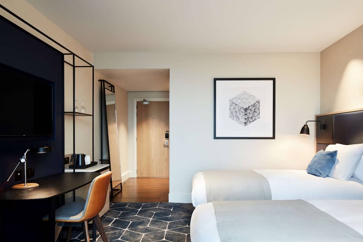 Ein Hotelzimmer mit einem Bett, einem Schreibtisch mit Stuhl, einem Fernseher und einem gerahmten Kunstwerk an der Wand.