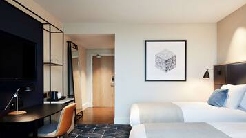 A hotel room with a bed, a desk with a chair, a TV, and a framed artwork on the wall.