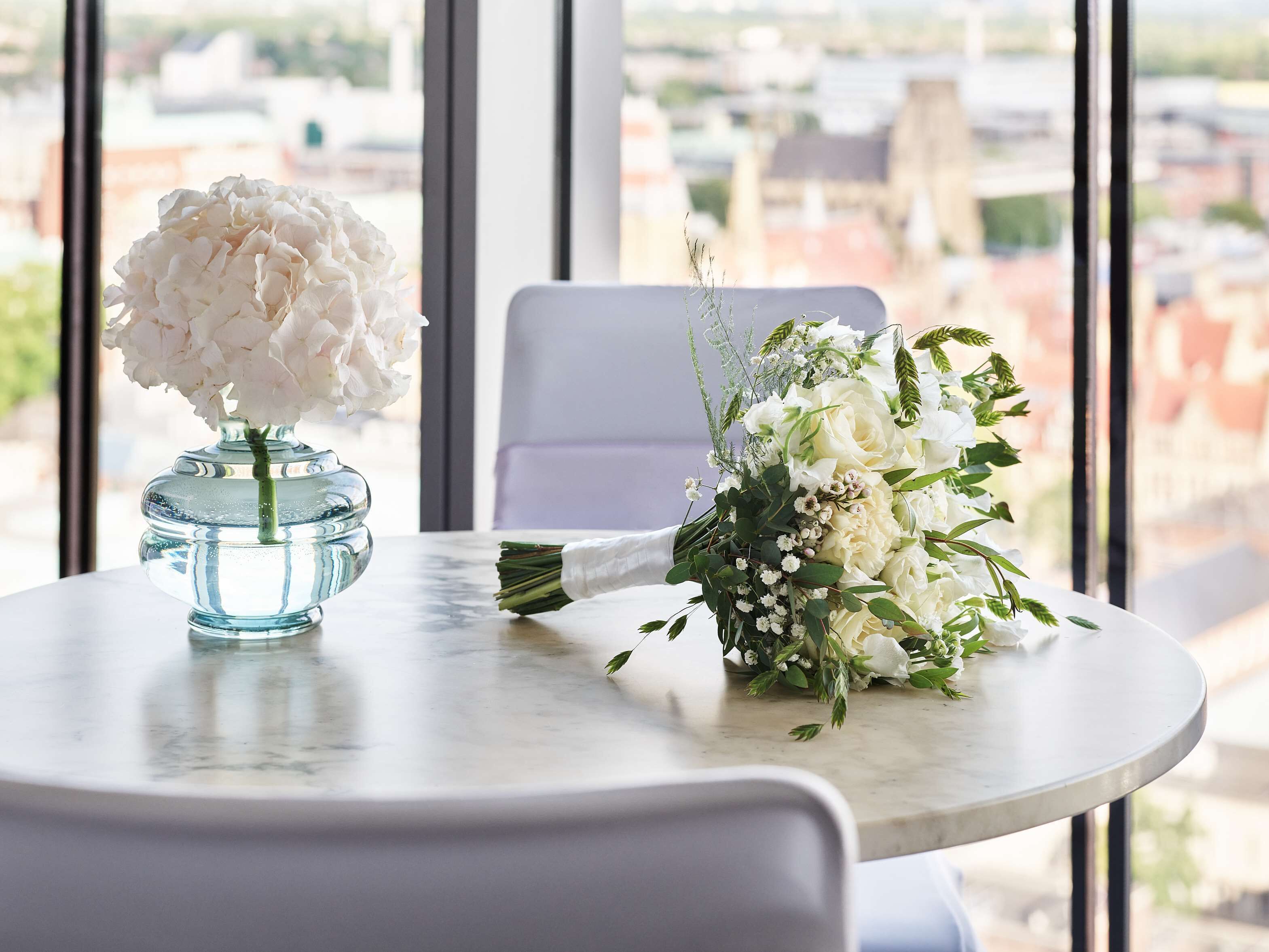 A table with a vase of white flowers and a bouquet of mixed flowers.