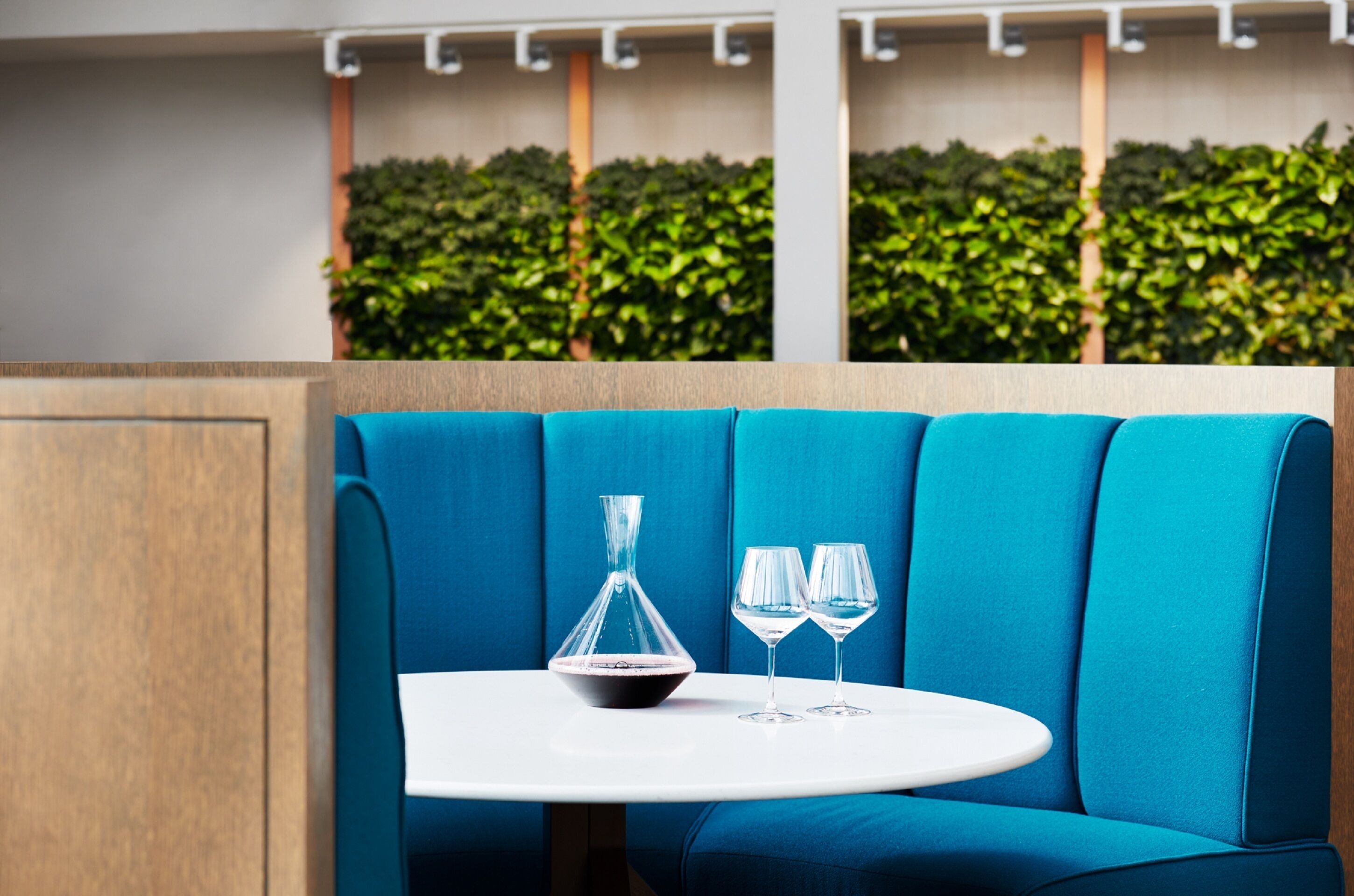 A blue cushioned seating area with a white table, a glass decanter, and two wine glasses.