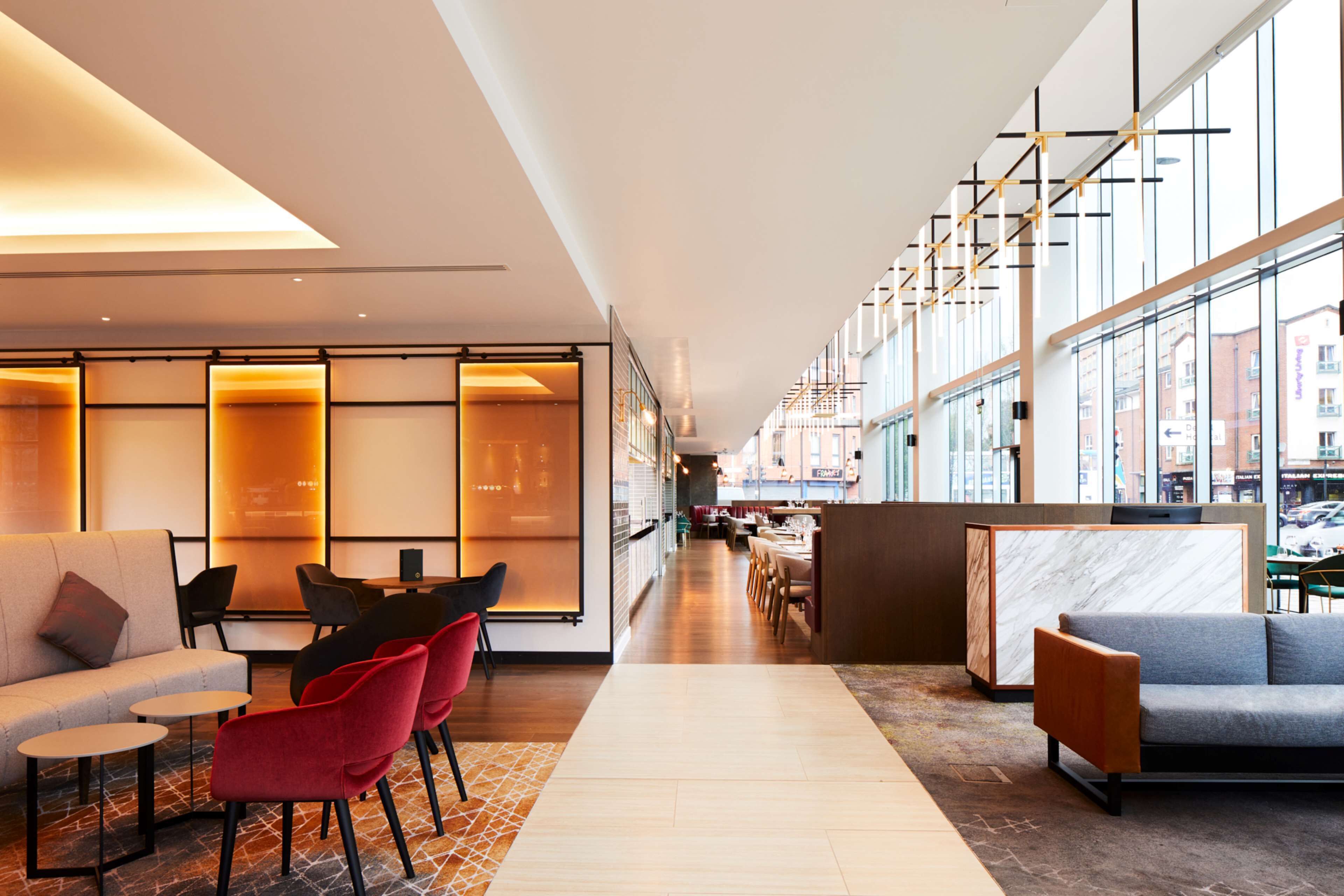 A modern hotel lobby with seating areas, a marble reception desk, and large windows offering city views.