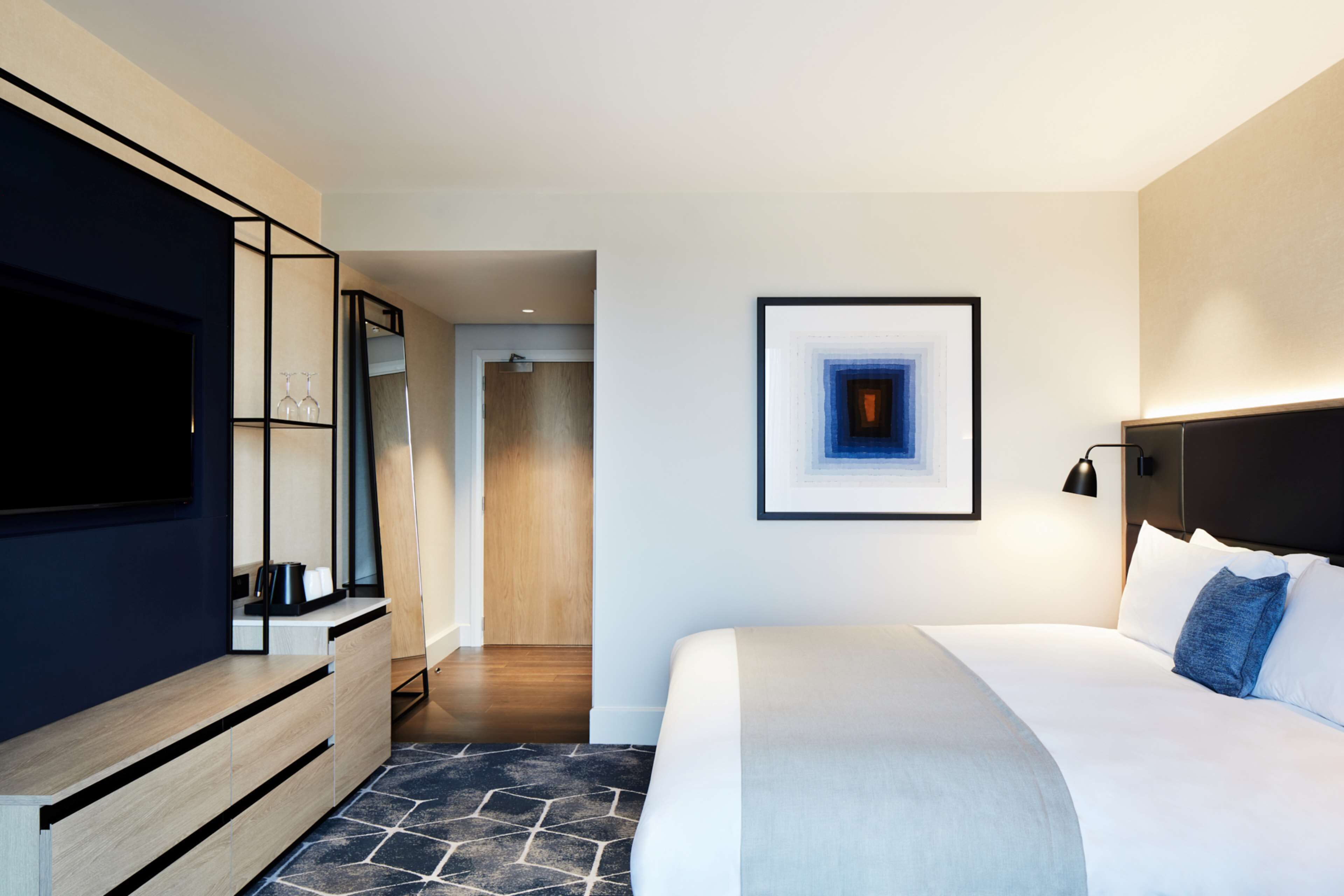 Habitación de hotel moderna con una cama grande, un televisor de pantalla plana, un mueble de madera y una obra de arte enmarcada en la pared.