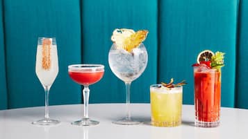 Cuatro cócteles diferentes en distintos vasos sobre una mesa, sobre un fondo verde azulado.