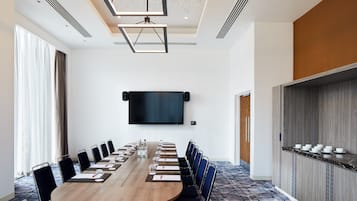 A conference room with a long table, chairs, a flat-screen TV, and a bar area with cups and glasses.