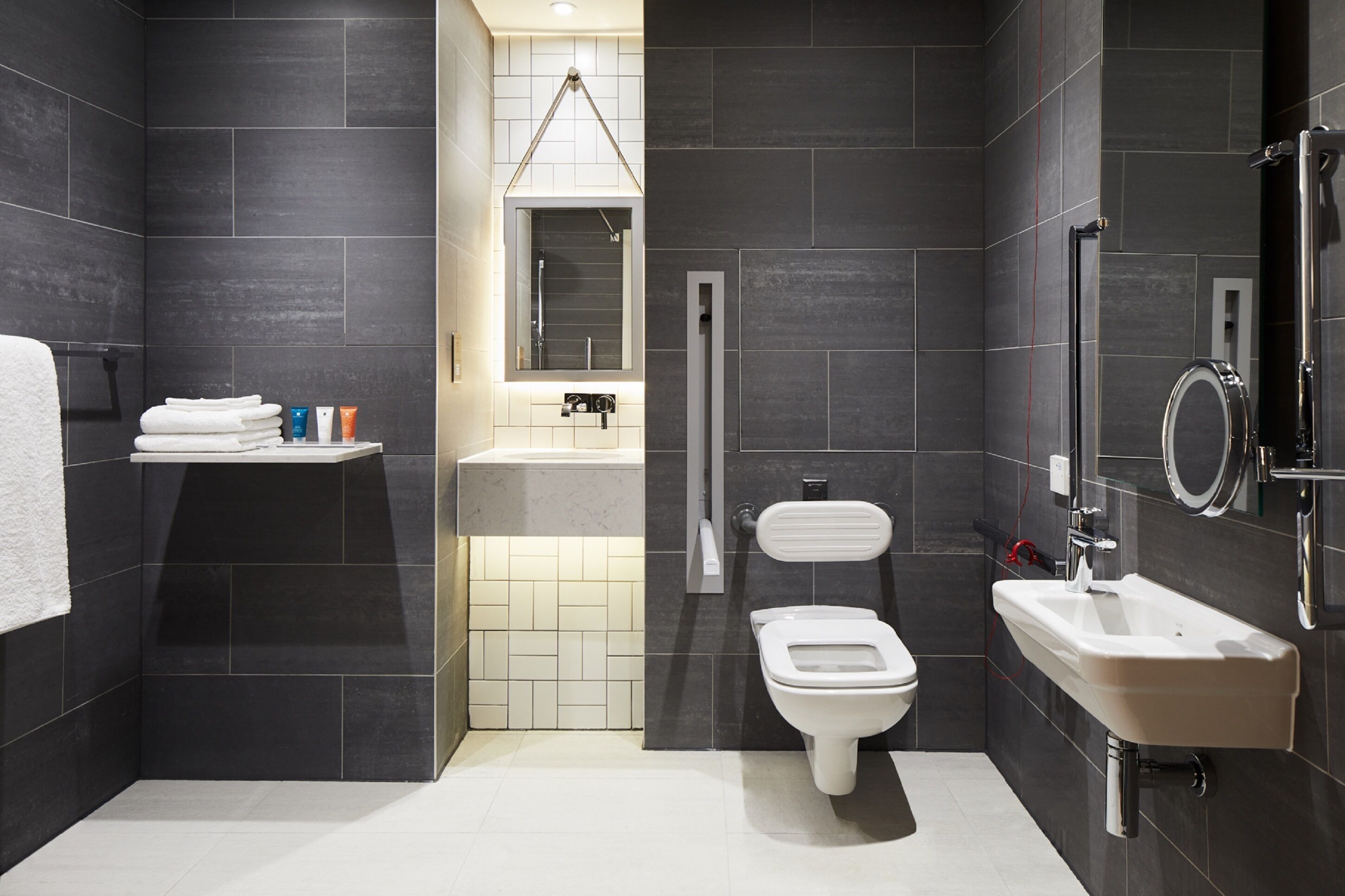 Une salle de bain moderne avec des carreaux de couleur sombre, des toilettes blanches, un lavabo et un miroir.