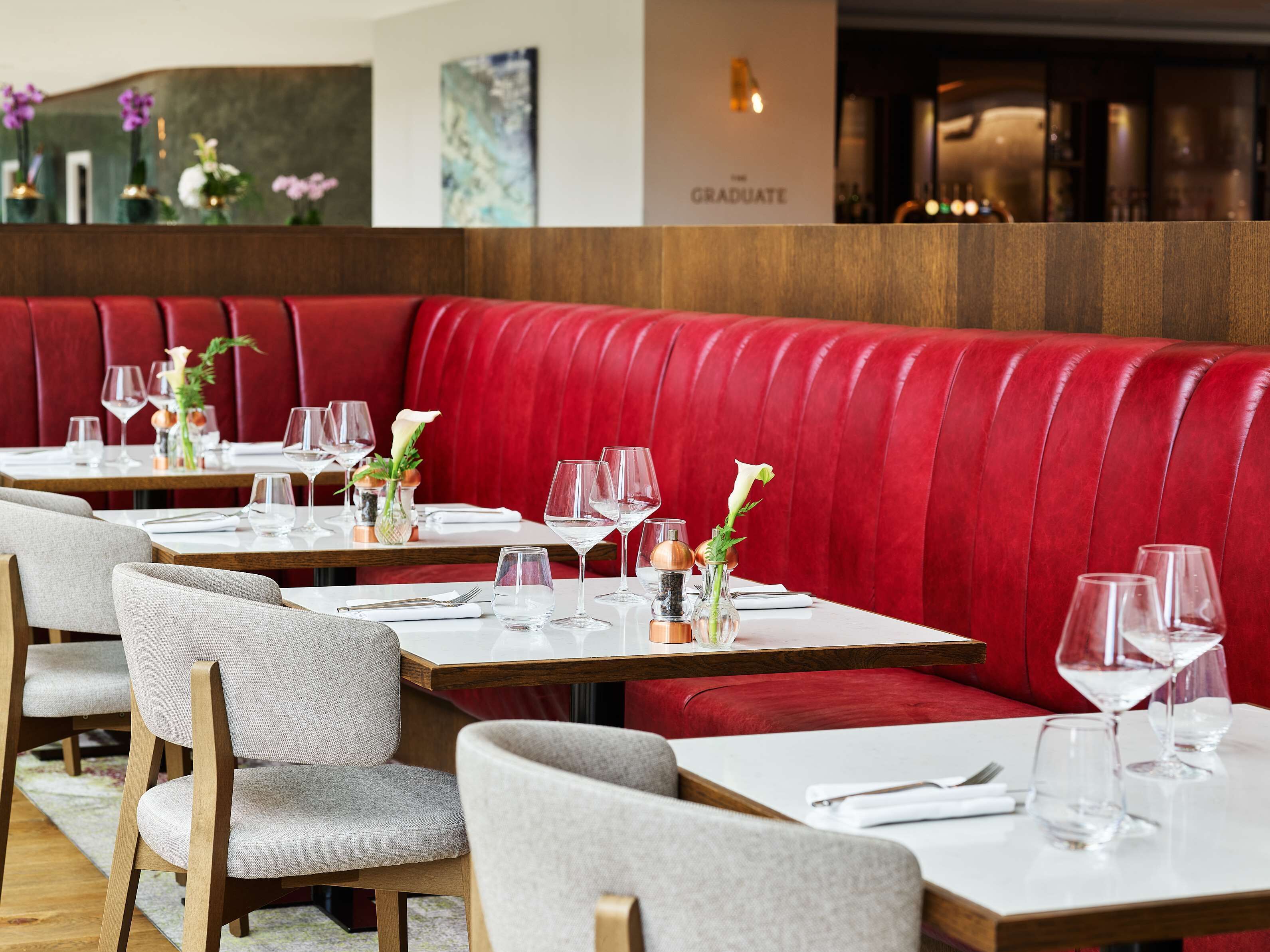A restaurant with red upholstered booths, white tables, and grey chairs.