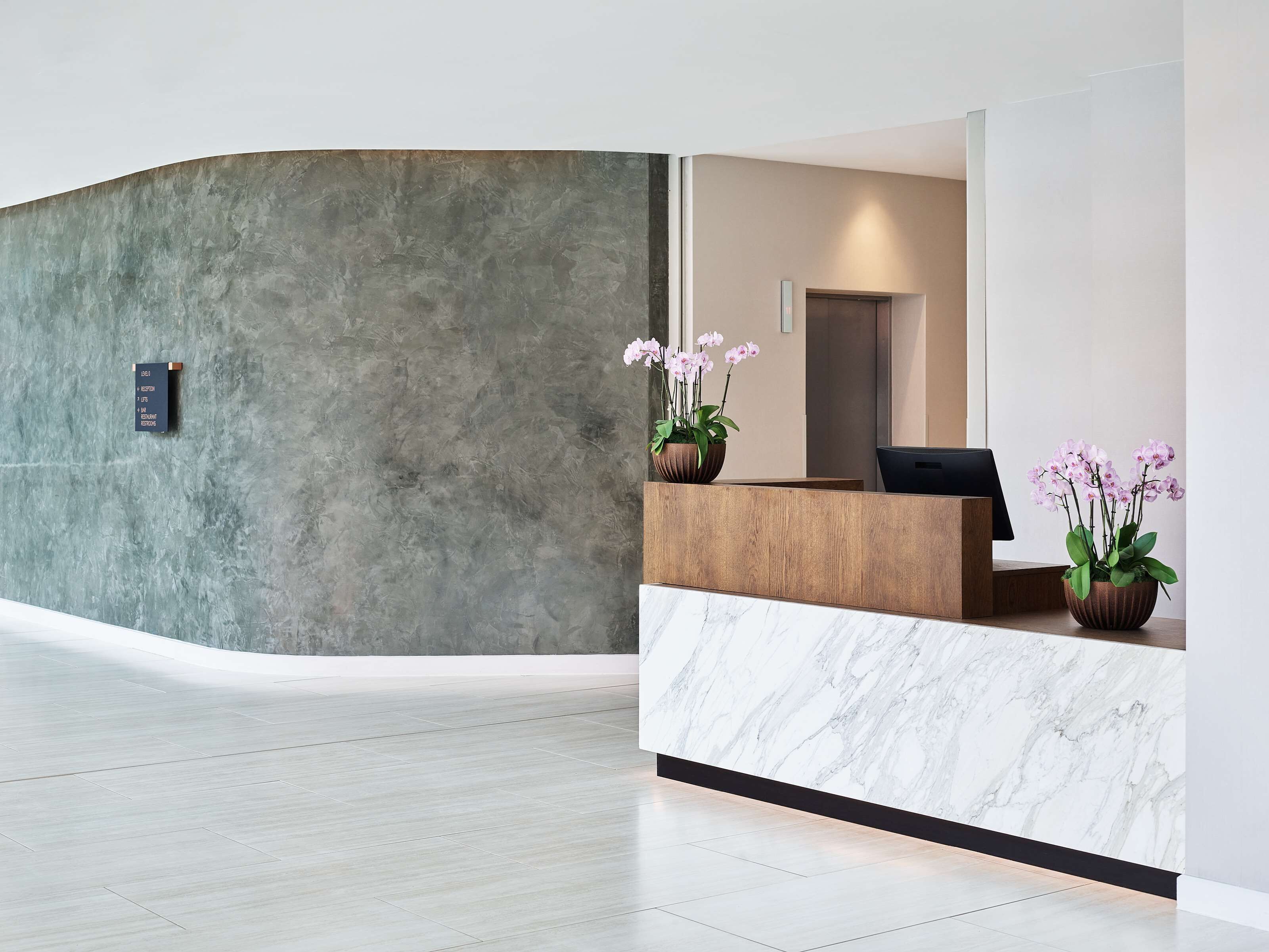 A modern reception area with a marble counter, potted orchids, and a concrete wall.