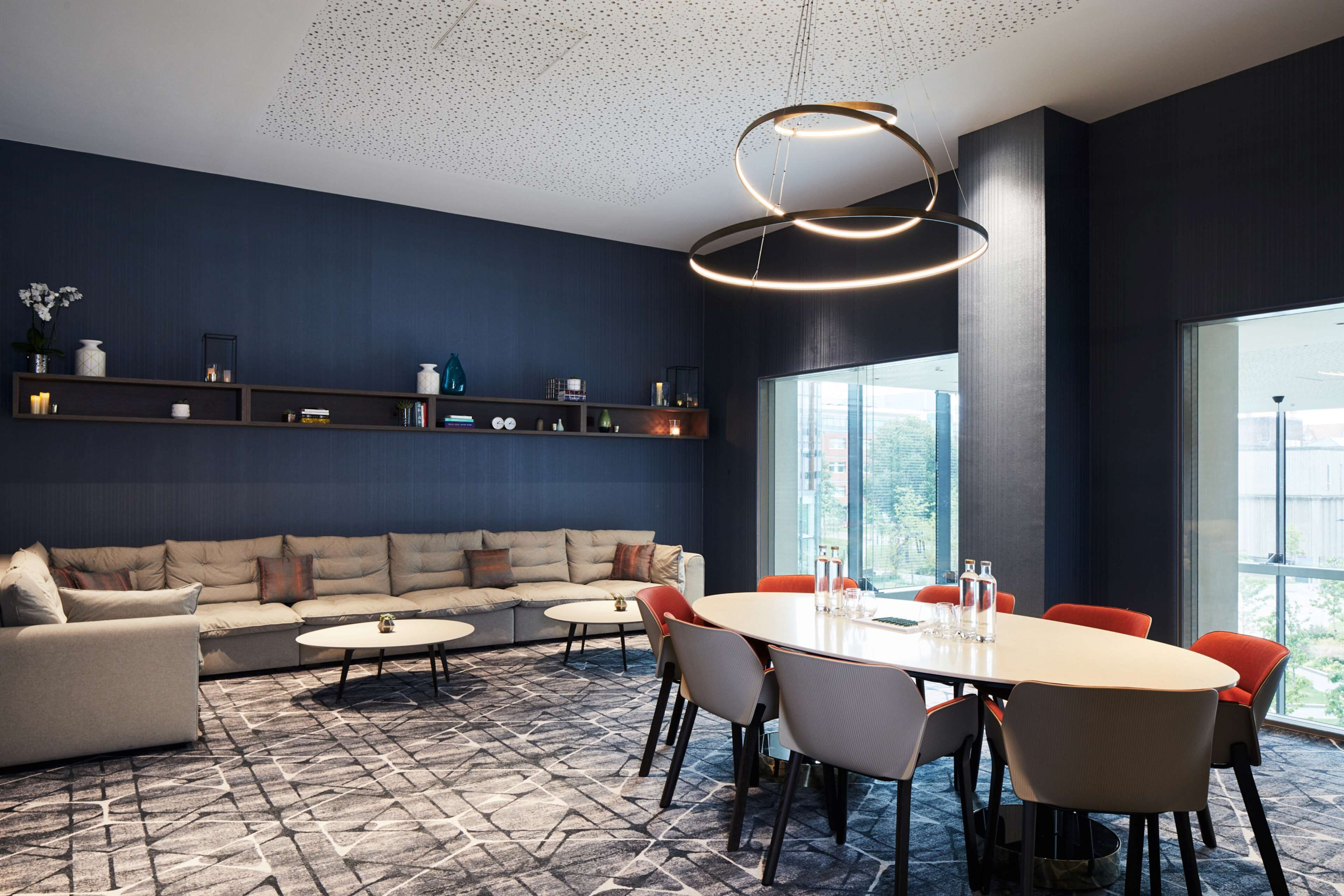 Una sala de reuniones moderna con una amplia mesa ovalada, asientos cómodos y una lámpara decorativa en el techo.
