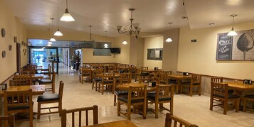Een ruim restaurant met houten tafels en stoelen, een kroonluchter en een bord met de tekst 'Café de Paris'.