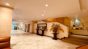 A spacious lobby with marble flooring, a staircase, and a reception desk with a vase of flowers. - Hotel Palace Puebla (Puebla)
