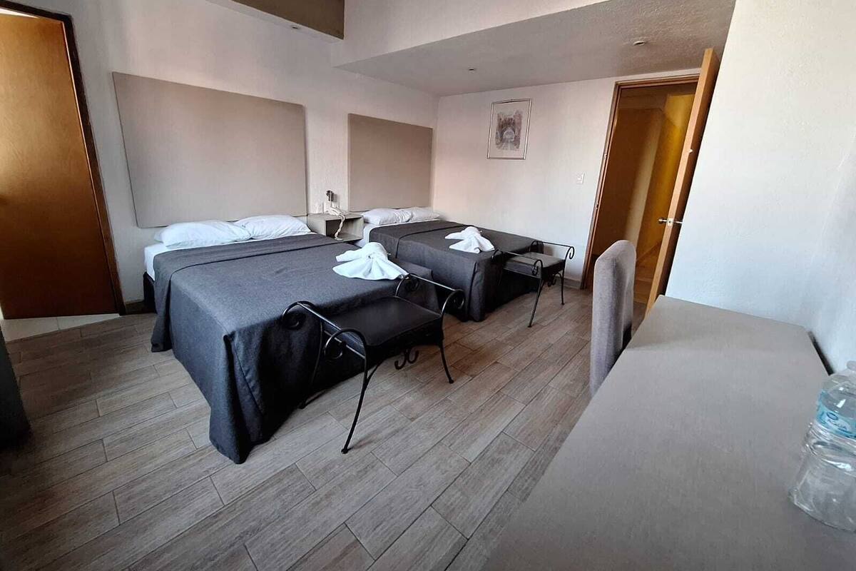 A hotel room with two single beds, a small table, and a chair.