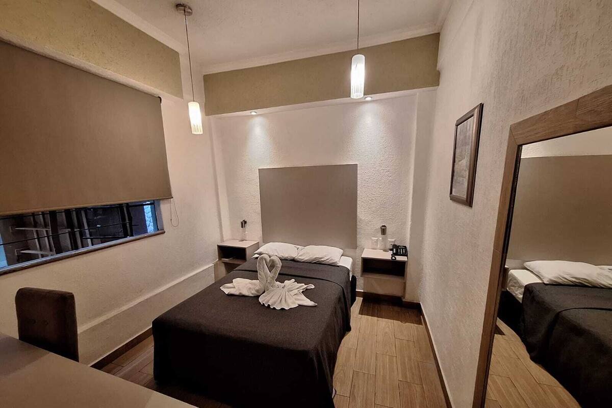 A hotel room with a bed, bedside tables, a mirror, and a window.