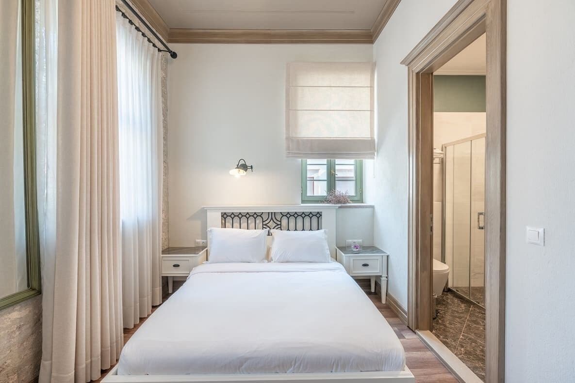 Un dormitorio con cama, mesitas de noche, una lámpara de pared y una ventana con persiana.