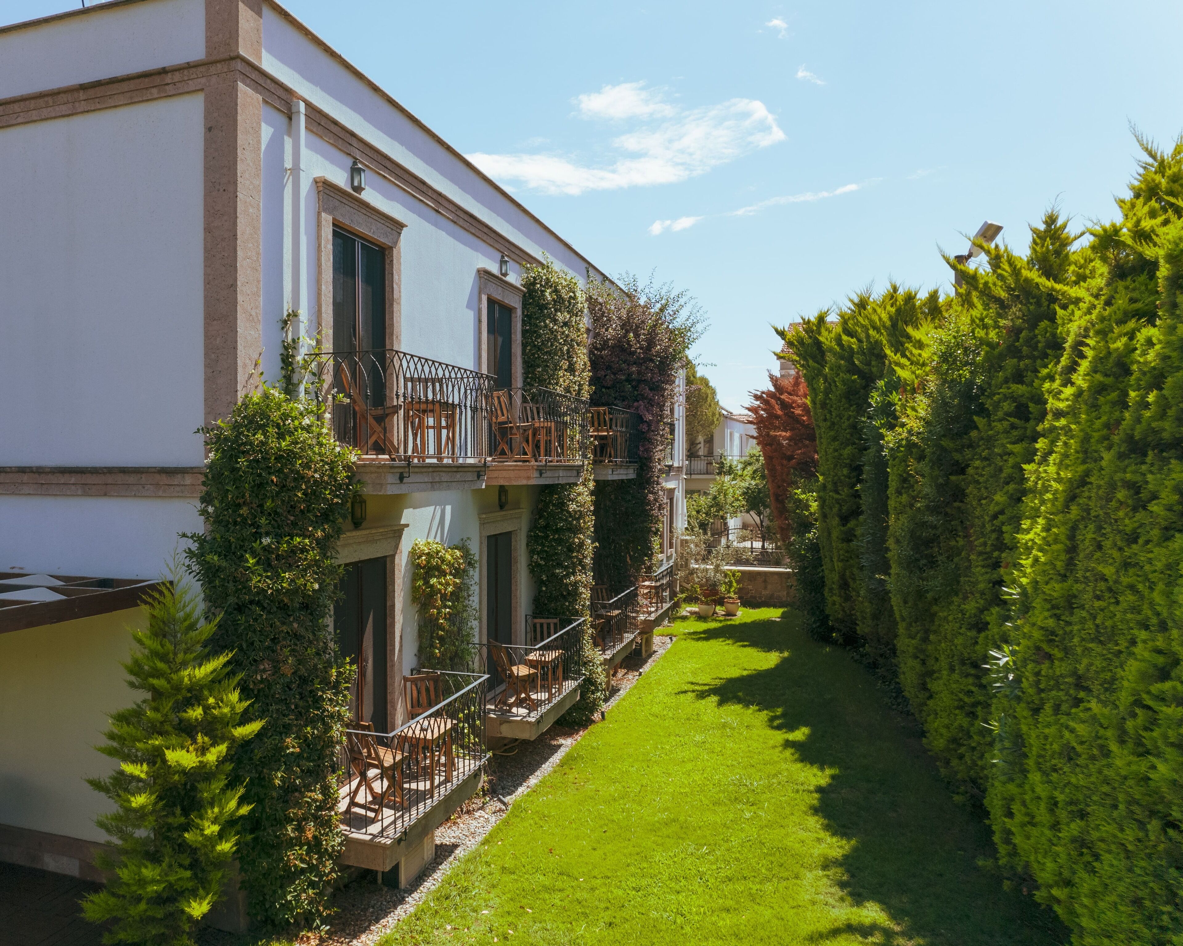 A building with a balcony, a well-maintained lawn, and dense greenery.