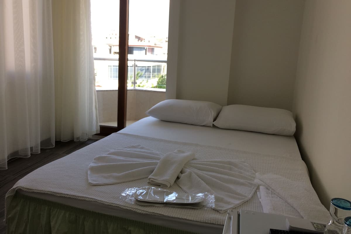 A hotel room with a bed, a window with curtains, and a view of buildings outside.