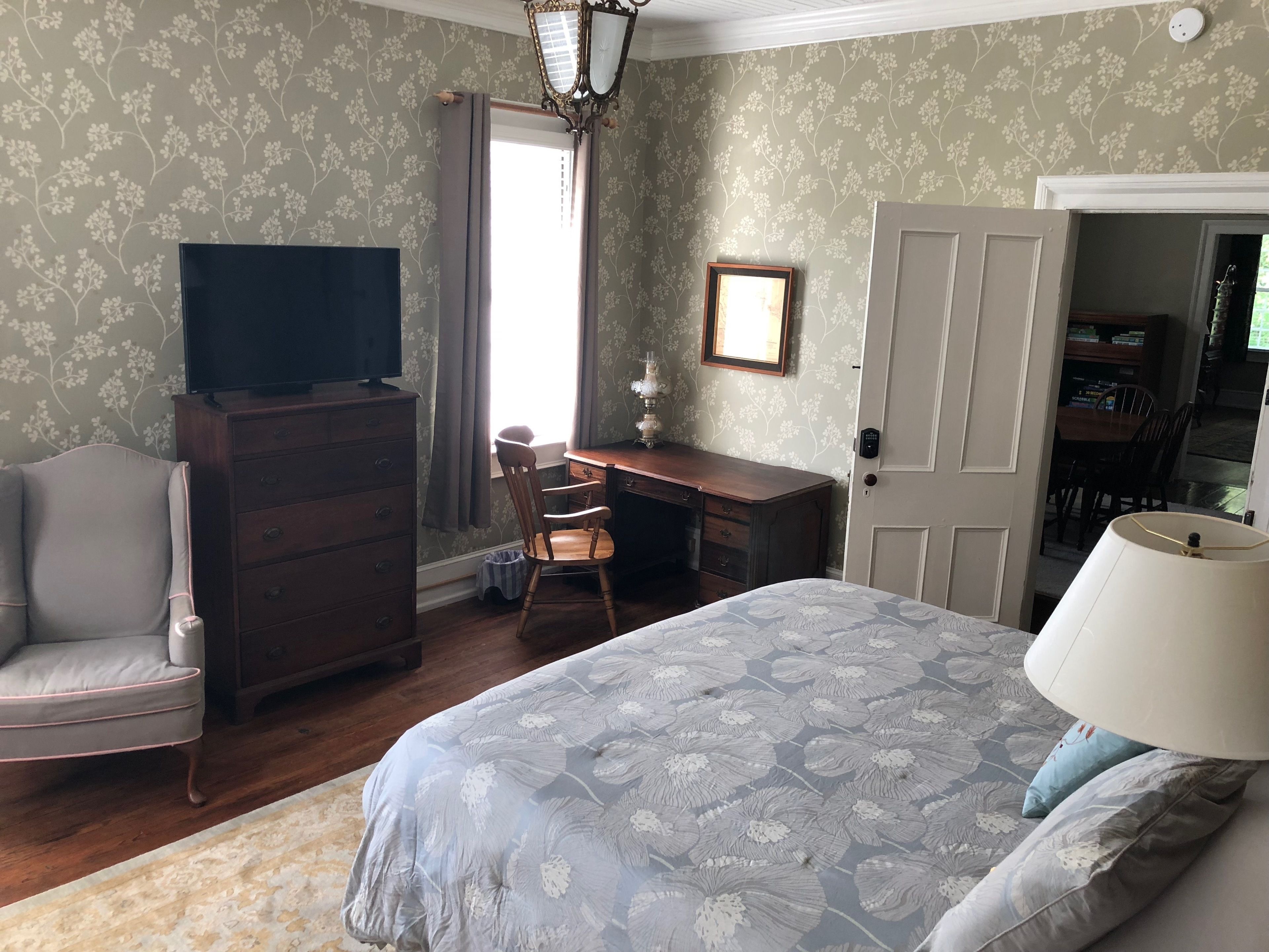 A bedroom with a bed, dresser, desk, chair, and a television.