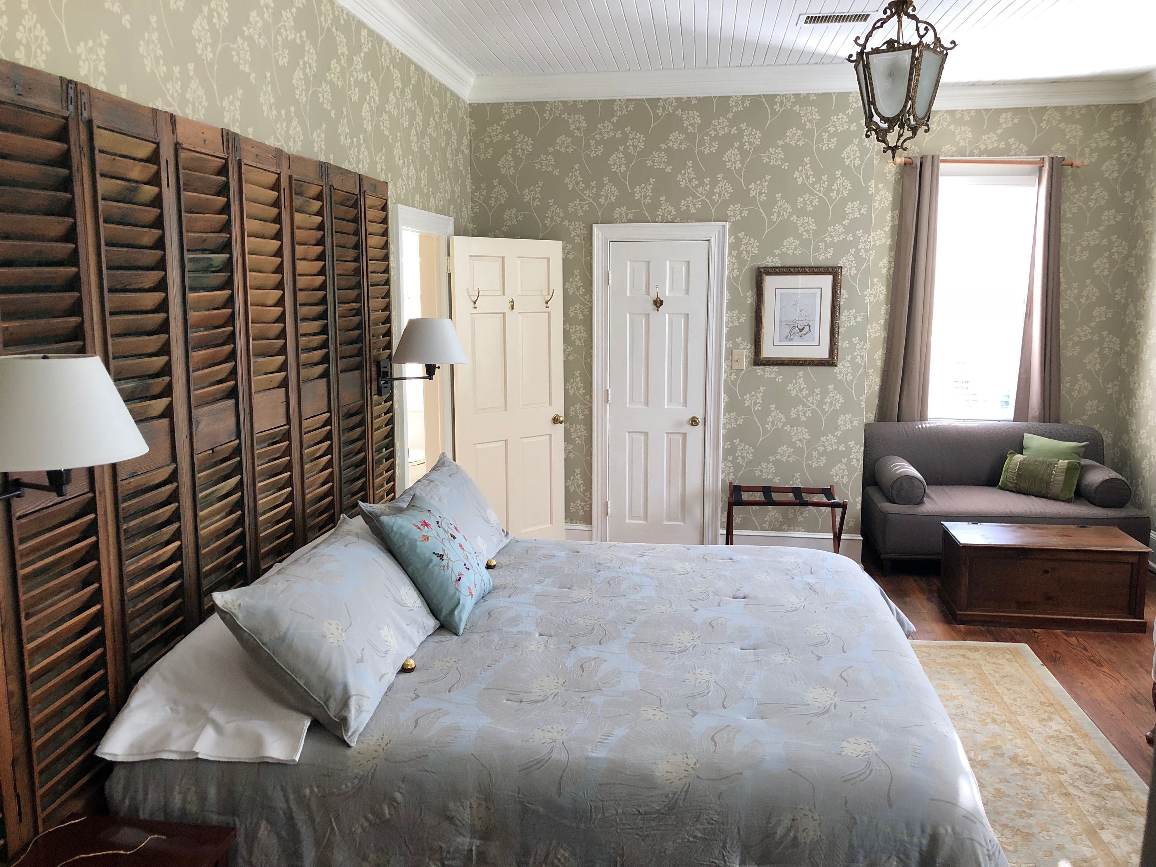 Un dormitorio con una cama grande, un sofá, una mesita y una silla. Hay dos puertas, una de las cuales está abierta.
