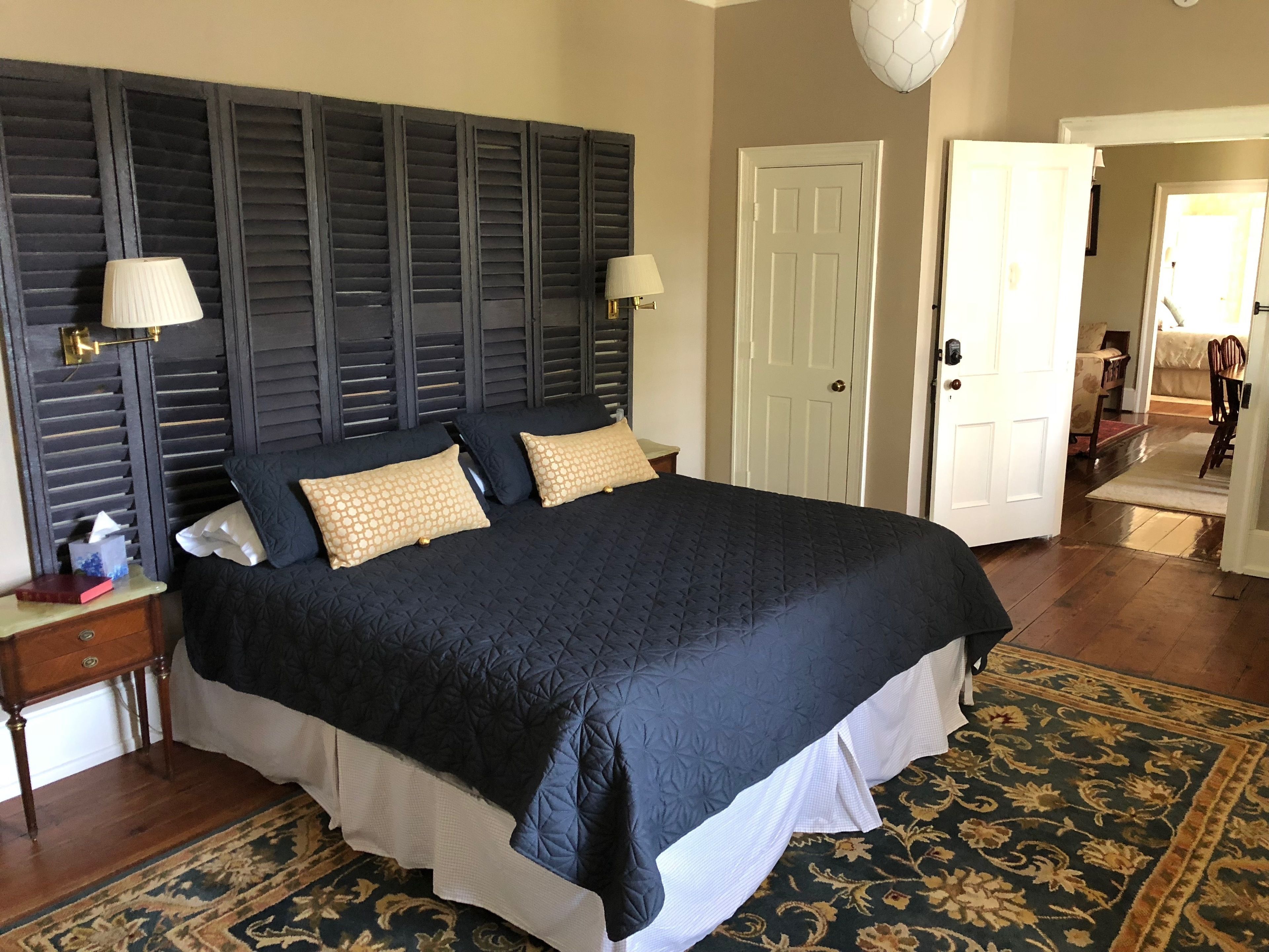 A large bed with a dark quilt, two bedside lamps, and a patterned rug.