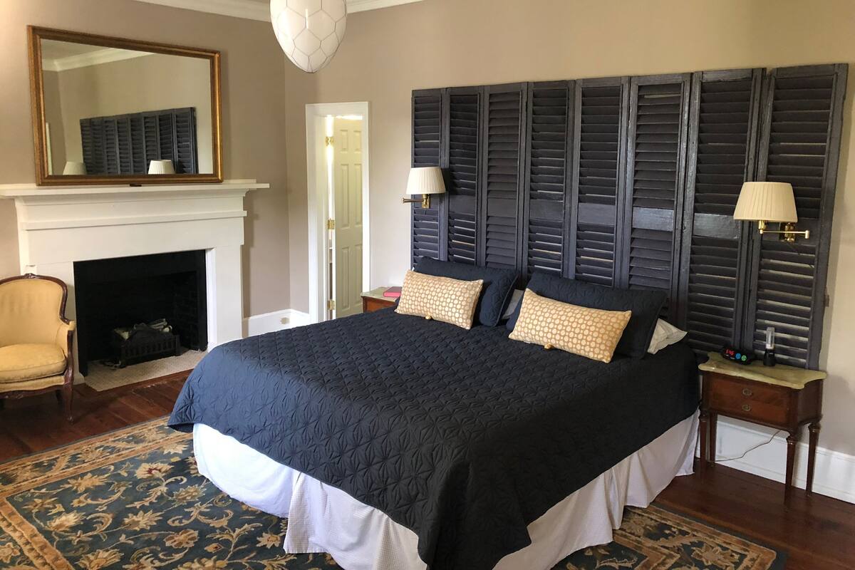 A bedroom with a large bed, a fireplace, a mirror, and two nightstands.