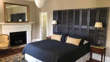 A bedroom with a large bed, a fireplace, a mirror, and two nightstands.