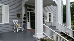 Eine Veranda mit weißen Geländern und einer Bank, eine Tür mit grüner Farbe und eine Plakette an der Wand.