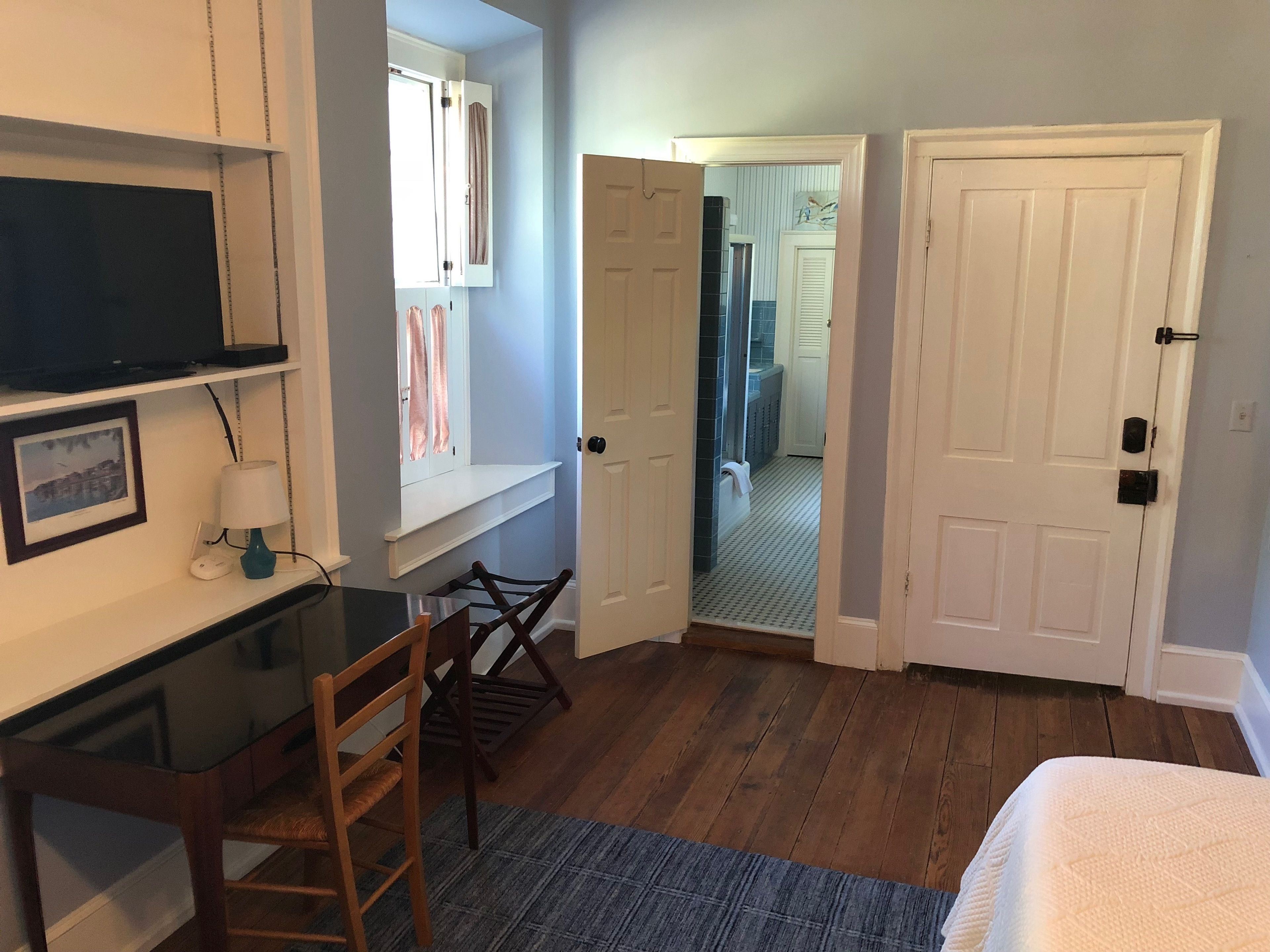A bedroom with a desk, chair, bed, and a door leading to another room.