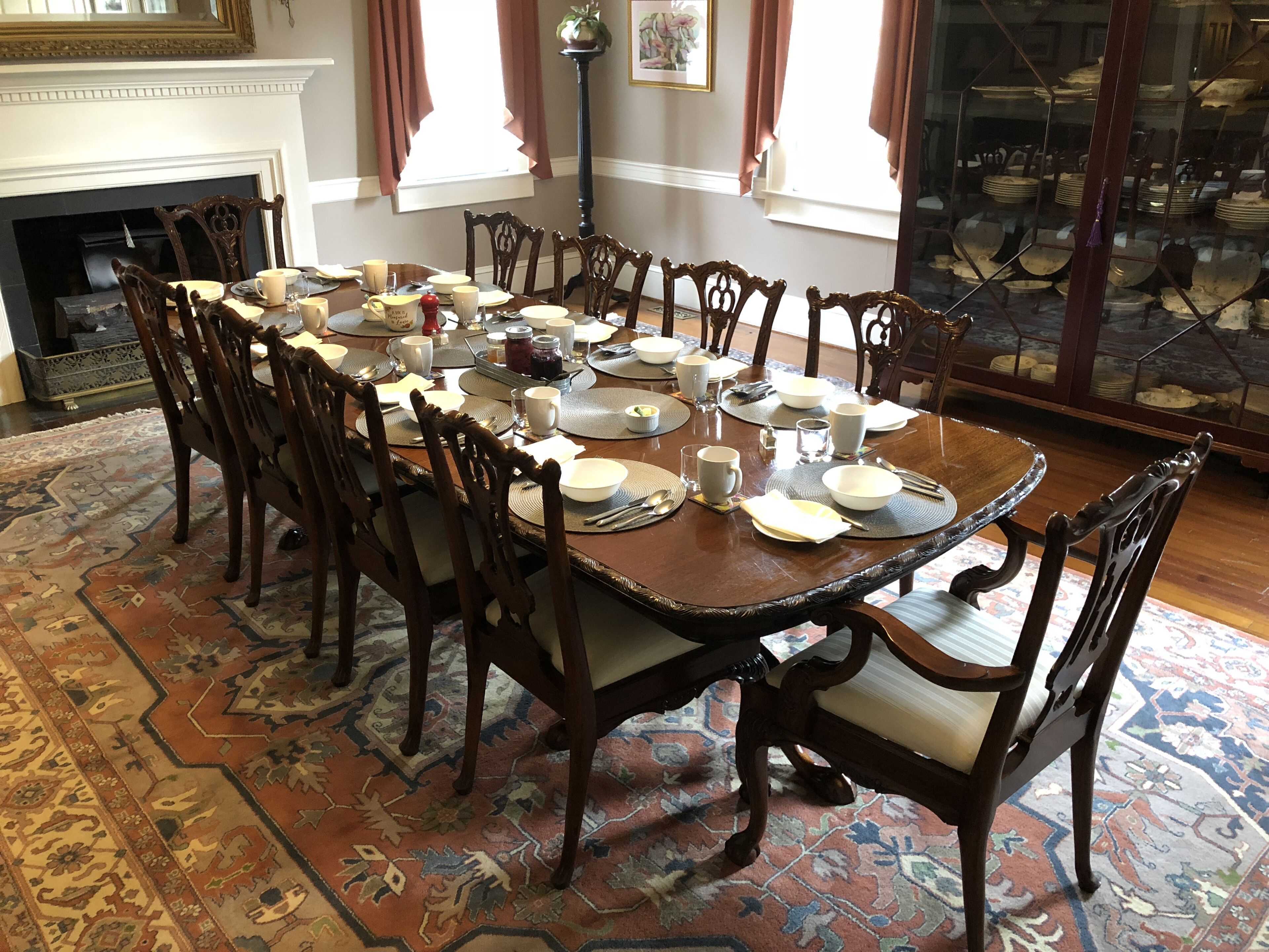 A dining room with a large wooden table set for a meal, surrounded by ornate chairs.
