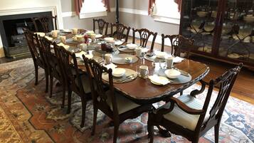 A dining room with a large wooden table set for a meal, surrounded by ornate chairs.