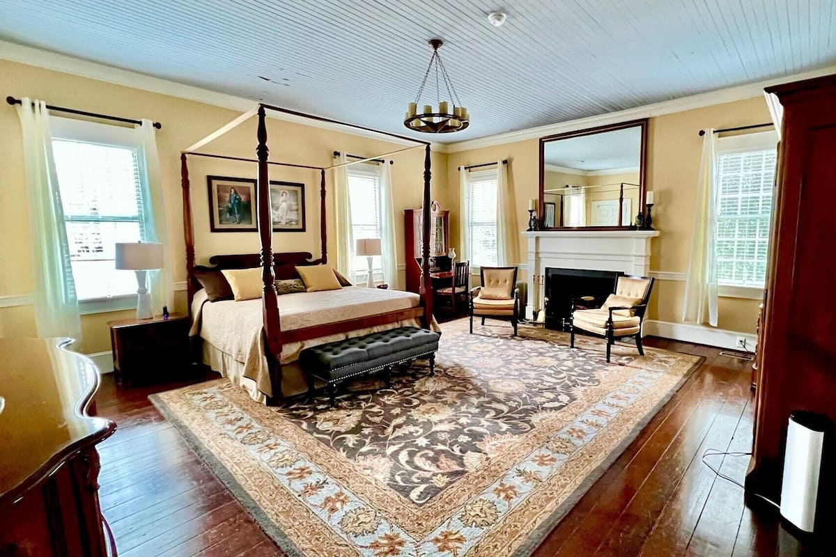 A spacious bedroom with a four-poster bed, a large ornate rug, and a fireplace.