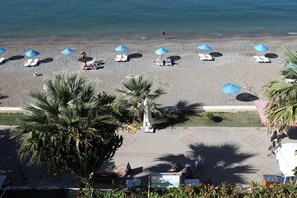 Una playa con filas de tumbonas y sombrillas, palmeras y una estatua en primer plano.