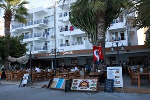 Un restaurante llamado "Simsek" con terraza, una bandera y una pizarra de menú.