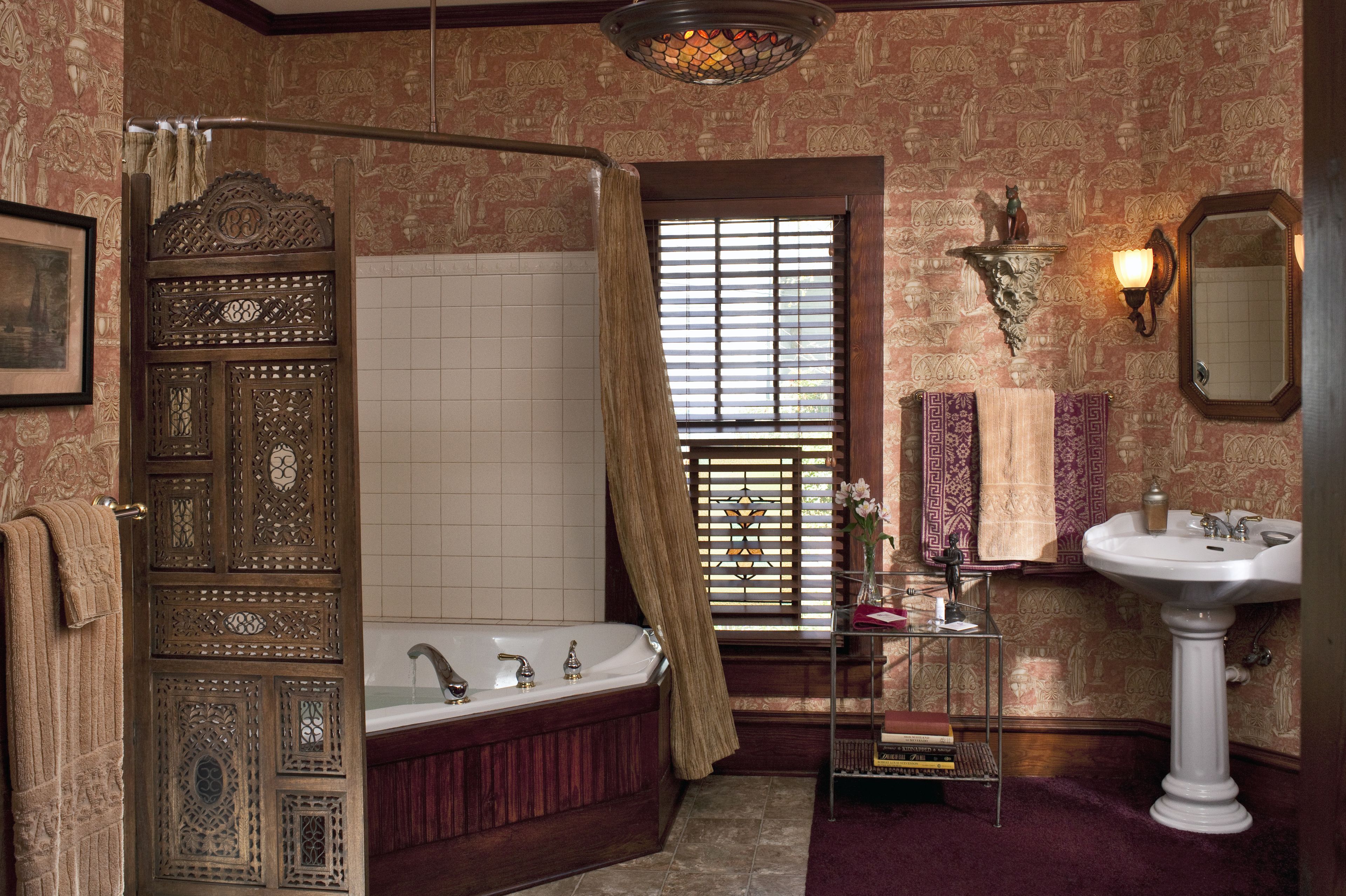 A bathroom with a freestanding bathtub, a pedestal sink, and a decorative mirror.